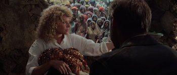 Movie still from “Indiana Jones and the Temple of Doom” (1984), directed by Steven Spielberg – A woman sitting in front of a group of people; Medium shot, Over the shoulder angle