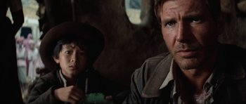 Movie still from “Indiana Jones and the Temple of Doom” (1984), directed by Steven Spielberg – A man and a boy are sitting in a room together; Close Up shot, Over the shoulder angle