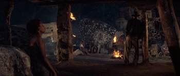 Movie still from “Indiana Jones and the Temple of Doom” (1984), directed by Steven Spielberg – A group of people sitting around a fire pit; Wide shot, Over the shoulder angle