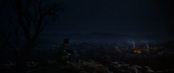 Movie still from “Indiana Jones and the Temple of Doom” (1984), directed by Steven Spielberg – A man sitting on top of a hill at night; Extreme Wide shot, High angle