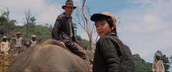 Movie still from “Indiana Jones and the Temple of Doom” (1984), directed by Steven Spielberg – A man sitting on top of an elephant with a young boy; Medium shot, Low angle