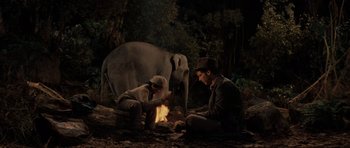 Movie still from “Indiana Jones and the Temple of Doom” (1984), directed by Steven Spielberg – Two men sitting on the ground near an elephant; Wide shot, High angle