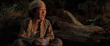 Movie still from “Indiana Jones and the Temple of Doom” (1984), directed by Steven Spielberg – A young boy sitting on the ground holding a piece of food; Close Up shot, High angle
