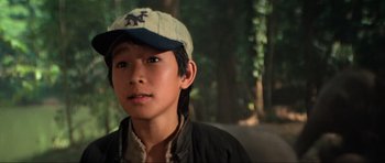 Movie still from “Indiana Jones and the Temple of Doom” (1984), directed by Steven Spielberg – A young boy wearing a baseball cap in the woods; Close Up shot, Over the shoulder angle