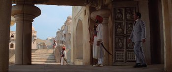 Movie still from “Indiana Jones and the Temple of Doom” (1984), directed by Steven Spielberg – A man in a turban stands in front of a building; Wide shot, Low angle