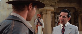 Movie still from “Indiana Jones and the Temple of Doom” (1984), directed by Steven Spielberg – A man with a hat and a sword standing in front of a man with a hat and a sword standing in front of another man; Medium shot, Over the shoulder angle
