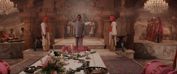 Movie still from “Indiana Jones and the Temple of Doom” (1984), directed by Steven Spielberg – A man standing in front of a table with candles; Wide shot, High angle
