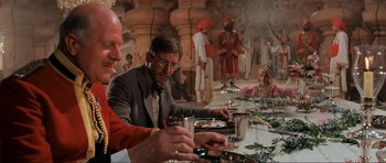 Movie still from “Indiana Jones and the Temple of Doom” (1984), directed by Steven Spielberg – A group of people sitting at a long table; Medium shot, Over the shoulder angle