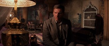 Movie still from “Indiana Jones and the Temple of Doom” (1984), directed by Steven Spielberg – A man in a suit and tie sitting on a bed; Medium shot, Low angle