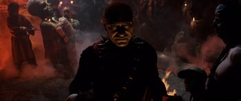 Movie still from “Indiana Jones and the Temple of Doom” (1984), directed by Steven Spielberg – A man in a black shirt and a red and black mask; Medium shot, High angle