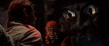 Movie still from “Indiana Jones and the Temple of Doom” (1984), directed by Steven Spielberg – A man with a bald head is looking at another man in a cave; Close Up shot, Over the shoulder angle
