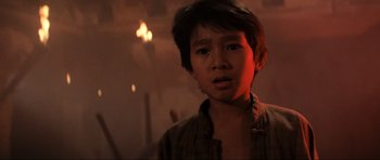 Movie still from “Indiana Jones and the Temple of Doom” (1984), directed by Steven Spielberg – A young asian boy standing in front of a fire; Close Up shot, Low angle