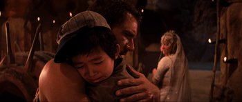 Movie still from “Indiana Jones and the Temple of Doom” (1984), directed by Steven Spielberg – A man and a boy hugging each other in front of a crowd; Close Up shot, Over the shoulder angle