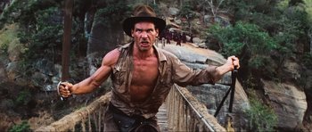 Movie still from “Indiana Jones and the Temple of Doom” (1984), directed by Steven Spielberg – A man in a hat and shirt is standing on a bridge; Medium shot, Low angle