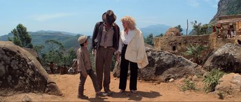 Movie still from “Indiana Jones and the Temple of Doom” (1984), directed by Steven Spielberg – A man , woman , and child standing on a dirt field; Wide shot, Low angle