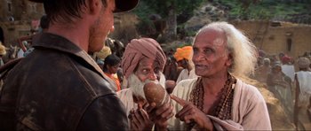 Movie still from “Indiana Jones and the Temple of Doom” (1984), directed by Steven Spielberg – A group of men standing around talking to each other; Medium shot, Over the shoulder angle