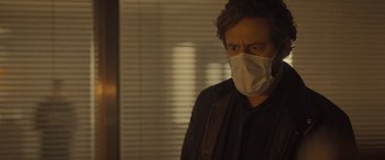 Movie still from “Infiesto” (2023), directed by Patxi Amezcua – A man wearing a face mask standing in front of a window; Close Up shot, Over the shoulder angle