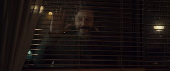 Movie still from “Infiesto” (2023), directed by Patxi Amezcua – A bearded man looking out of a window through blinds; Medium shot, Low angle