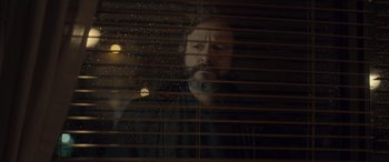 Movie still from “Infiesto” (2023), directed by Patxi Amezcua – A man looking out of a window through blinds; Close Up shot, Low angle