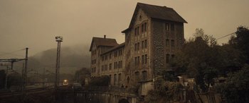 Movie still from “Infiesto” (2023), directed by Patxi Amezcua – An old brick building with many windows on a foggy day; Extreme Wide shot, High angle