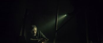 Movie still from “Infiesto” (2023), directed by Patxi Amezcua – A man holding a gun in a dark room; Medium shot, Low angle