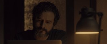 Movie still from “Infiesto” (2023), directed by Patxi Amezcua – A man with a beard is looking at a laptop; Close Up shot, Low angle