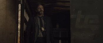 Movie still from “Infiesto” (2023), directed by Patxi Amezcua – A man in a suit and tie standing in a dark room; Medium shot, Low angle