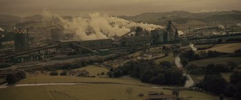 Movie still from “Infiesto” (2023), directed by Patxi Amezcua – An aerial view of an industrial area with smoke billowing out of the stacks; Extreme Wide shot, High angle