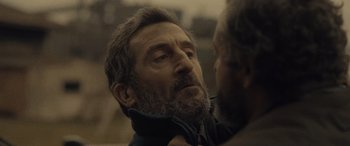 Movie still from “Infiesto” (2023), directed by Patxi Amezcua – An older man with a goatee and a beard; Close Up shot, Over the shoulder angle