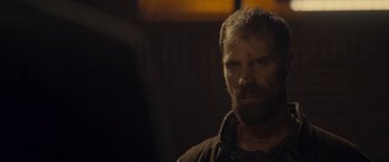 Movie still from “Infiesto” (2023), directed by Patxi Amezcua – A man with a shaggy beard is standing in a dark room; Close Up shot, Over the shoulder angle