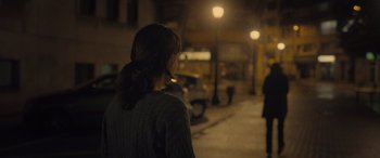 Movie still from “Infiesto” (2023), directed by Patxi Amezcua – A woman standing on the side of the street at night; Medium shot, Over the shoulder angle