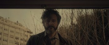 Movie still from “Infiesto” (2023), directed by Patxi Amezcua – A man with a beard is standing in front of some trees; Close Up shot, Low angle