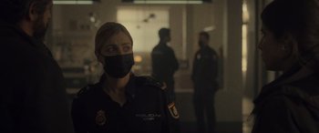 Movie still from “Infiesto” (2023), directed by Patxi Amezcua – A police officer wearing a mask in a dark room; Medium shot, Over the shoulder angle