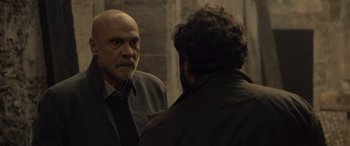Movie still from “Infiesto” (2023), directed by Patxi Amezcua – A man with a shaved head talking to another man in front of a brick wall; Medium shot, Over the shoulder angle