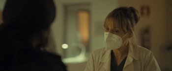 Movie still from “Infiesto” (2023), directed by Patxi Amezcua – A woman wearing a white lab coat and a face mask; Close Up shot, Over the shoulder angle