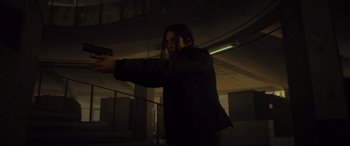 Movie still from “Infiesto” (2023), directed by Patxi Amezcua – A woman is holding a gun in a dark room; Medium shot, Low angle
