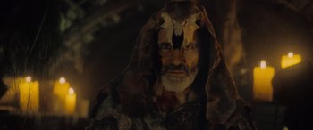 Movie still from “Infiesto” (2023), directed by Patxi Amezcua – An old man with a long beard and a mask on his face; Close Up shot, Low angle