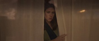 Movie still from “Infiesto” (2023), directed by Patxi Amezcua – A woman peeks out from behind a curtain; Medium shot, Low angle