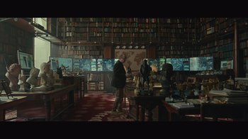 Movie still from “Infinite” (2021), directed by Antoine Fuqua – A man standing in front of a bookshelf in a room; Wide shot, High angle