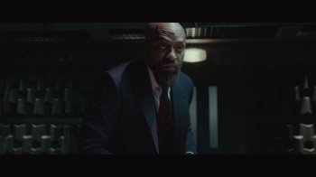 Movie still from “Infinite” (2021), directed by Antoine Fuqua – A man wearing a suit and tie in a dark room; Medium shot, Low angle