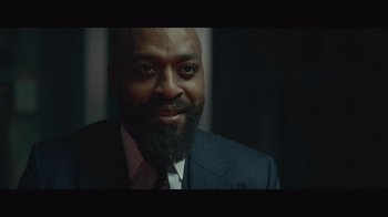 Movie still from “Infinite” (2021), directed by Antoine Fuqua – A man in a suit and tie smiling for the camera; Close Up shot, Low angle