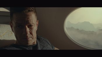 Movie still from “Infinite” (2021), directed by Antoine Fuqua – A man sitting in front of an airplane window; Medium shot, Low angle
