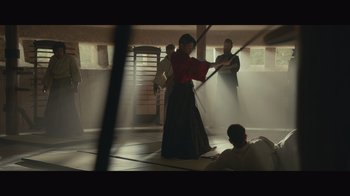 Movie still from “Infinite” (2021), directed by Antoine Fuqua – A woman in a red shirt is holding a sword; Wide shot, Low angle