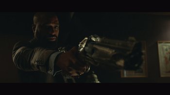 Movie still from “Infinite” (2021), directed by Antoine Fuqua – A man holding a gun in a dark room; Medium shot, Low angle