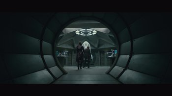 Movie still from “Infinite” (2021), directed by Antoine Fuqua – Two people are walking through a tunnel in a building; Wide shot, Overhead angle
