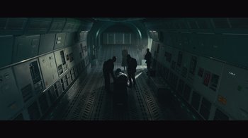 Movie still from “Infinite” (2021), directed by Antoine Fuqua – A group of men standing around a body in a dark room; Extreme Wide shot, High angle
