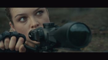 Movie still from “Infinite” (2021), directed by Antoine Fuqua – A woman is aiming a rifle in a field; Close Up shot, Over the shoulder angle