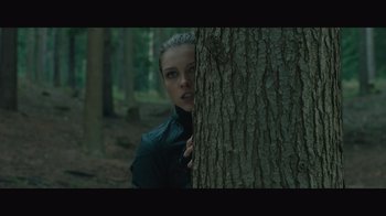 Movie still from “Infinite” (2021), directed by Antoine Fuqua – A woman hiding behind a tree in the woods; Medium shot, Low angle