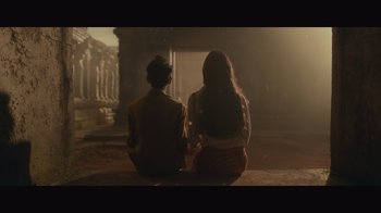 Movie still from “Infinite” (2021), directed by Antoine Fuqua – Two people sitting on the ground in front of a building; Wide shot, Low angle