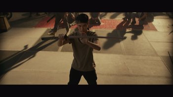 Movie still from “Infinite” (2021), directed by Antoine Fuqua – A man holding a sword while standing on the street; Medium shot, High angle